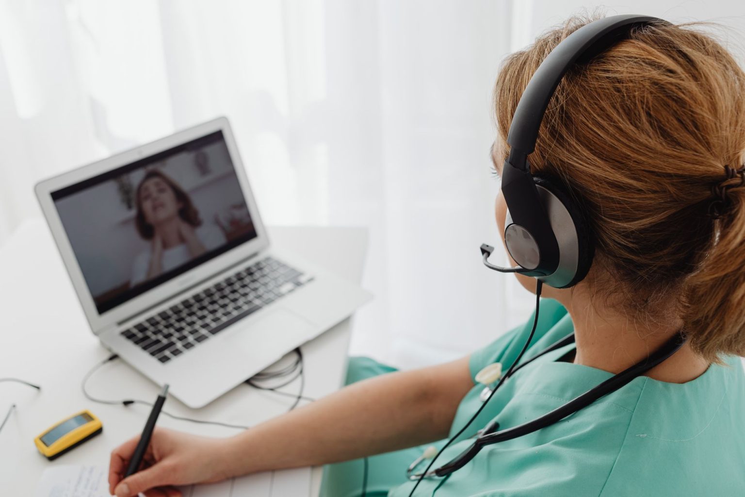 Profissional de saúde realiza uma consulta médica por videochamada com uma paciente usando um laptop.