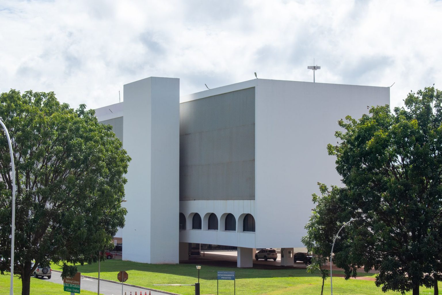 Edifício público branco de arquitetura moderna cercado por vegetação sob céu azul.