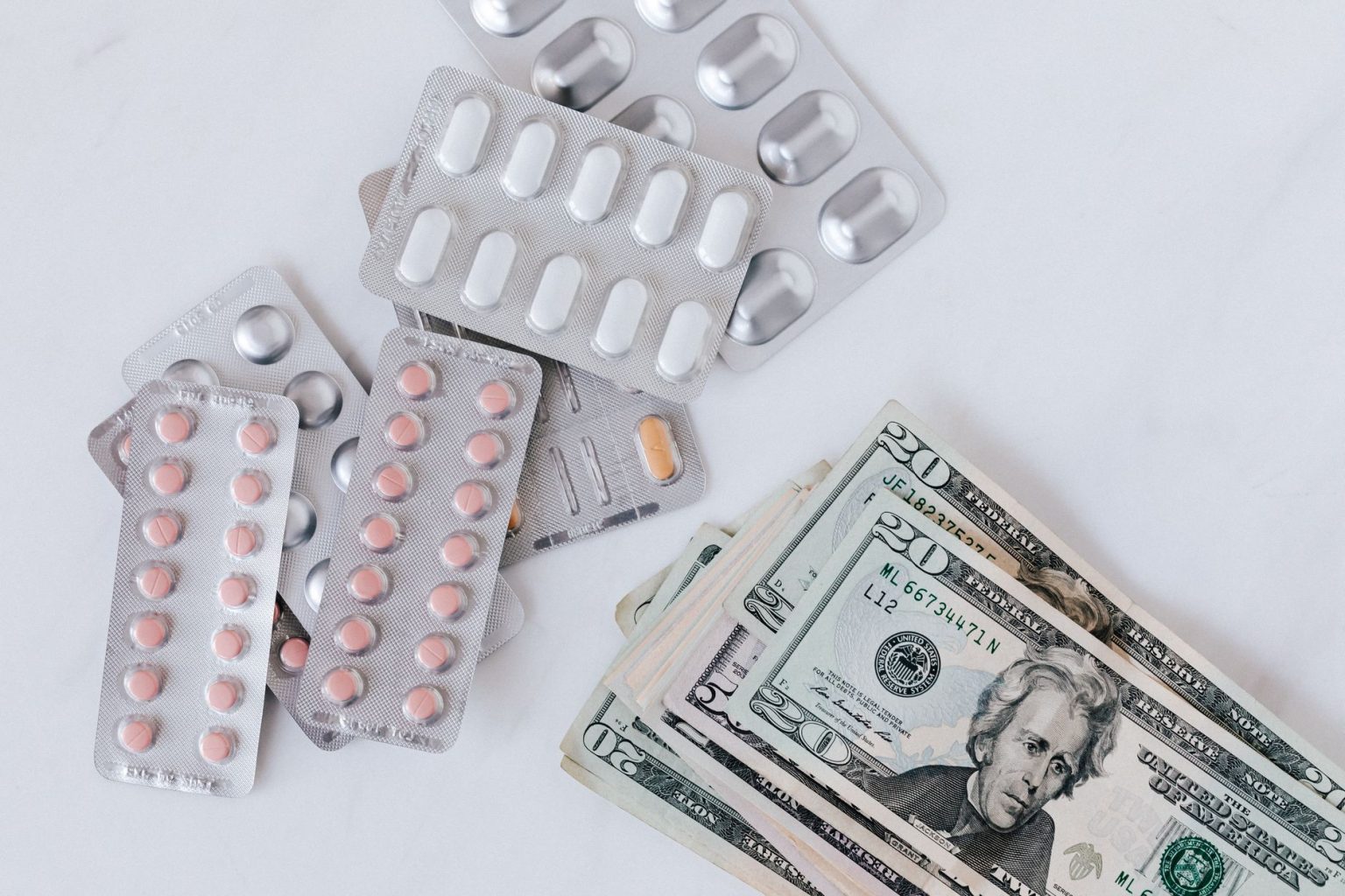 Blisters de medicamentos e comprimidos dispostos sobre uma pilha de cédulas, vistos de cima.