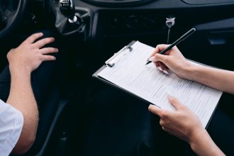 Pessoa preenche documentos em uma prancheta dentro de um carro, ao lado do câmbio