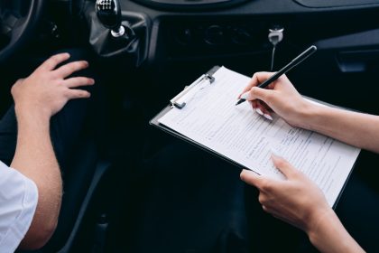 Pessoa preenche documentos em uma prancheta dentro de um carro, ao lado do câmbio