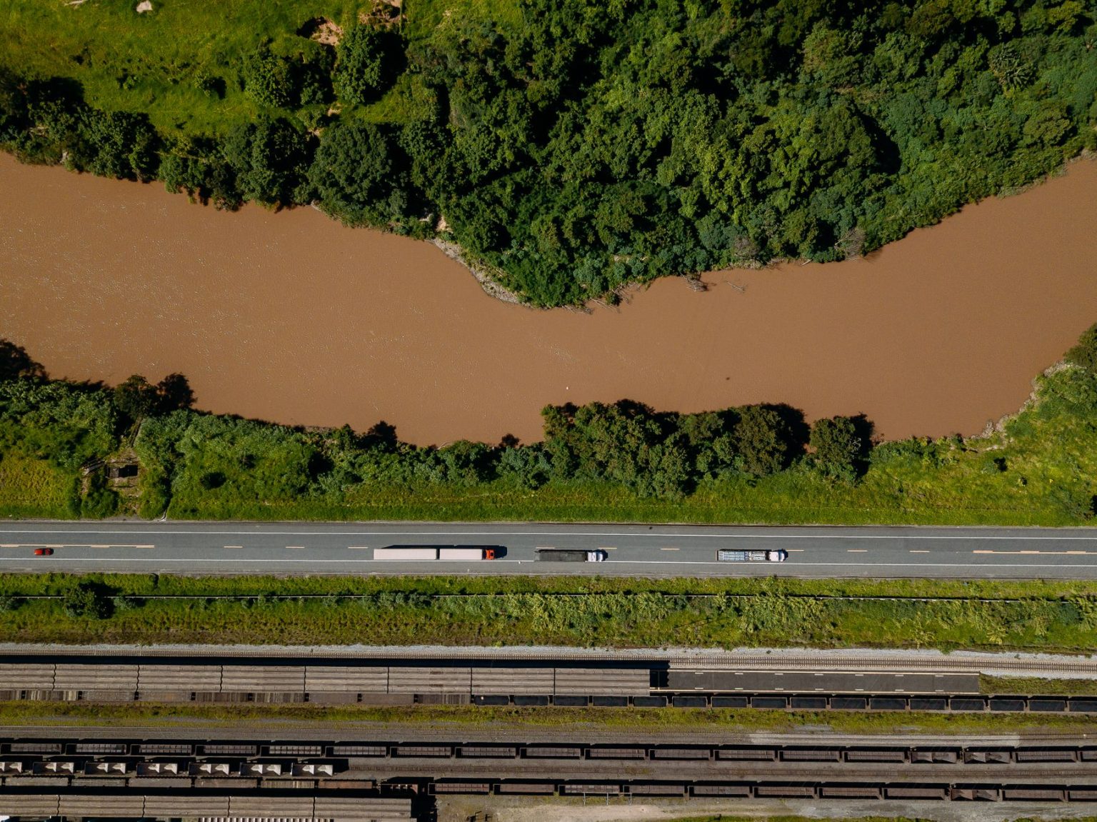 Vista aérea de caminhões trafegando por uma rodovia às margens de um rio no Brasil.
