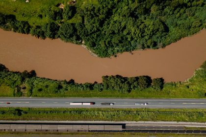 Vista aérea de caminhões trafegando por uma rodovia às margens de um rio no Brasil.