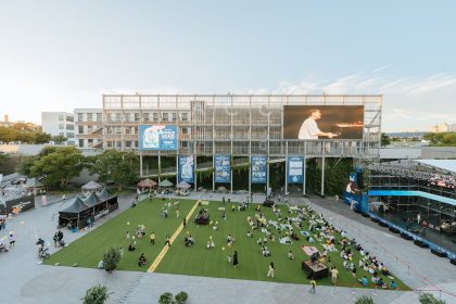 Público acompanha um concerto ao ar livre em uma praça durante o fim da tarde.