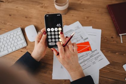 Mãos usando um aplicativo de calculadora no celular sobre documentos financeiros.