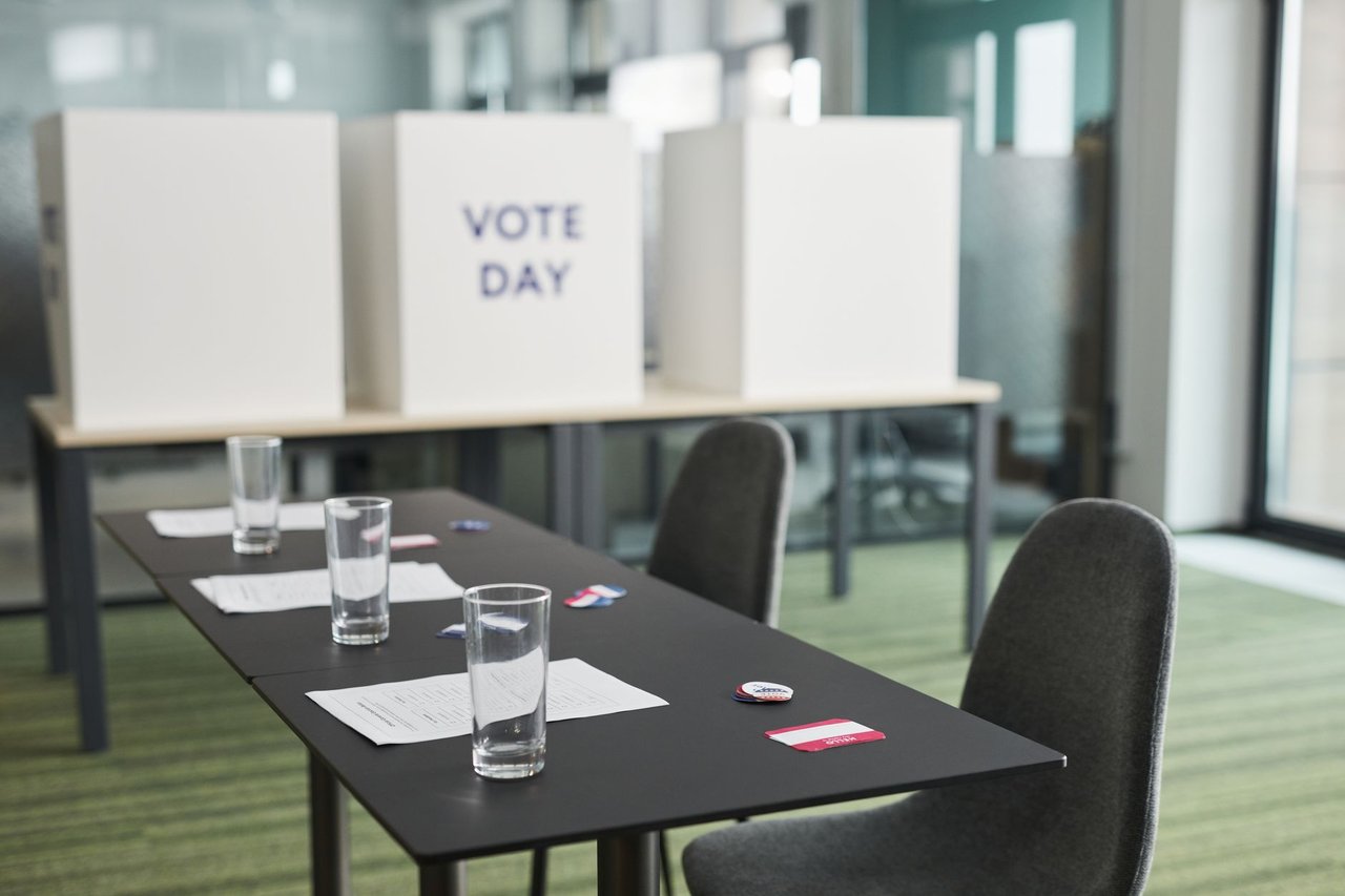 Seção eleitoral preparada, com mesas, cadeiras e cabines de votação em uma sala.