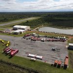 Vista aérea de uma base de combate a incêndios com caminhões, helicópteros e aviões de emergência.