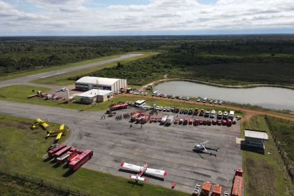 Vista aérea de uma base de combate a incêndios com caminhões, helicópteros e aviões de emergência.