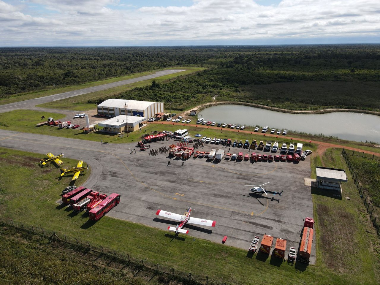 Vista aérea de uma base de combate a incêndios com caminhões, helicópteros e aviões de emergência.