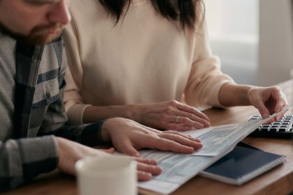 Homem e mulher analisam documentos financeiros à mesa, em casa, ao lado de um teclado e uma xícara de café.