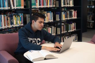 Estudante usa laptop e livros para estudar e realizar pesquisas em uma biblioteca universitária.