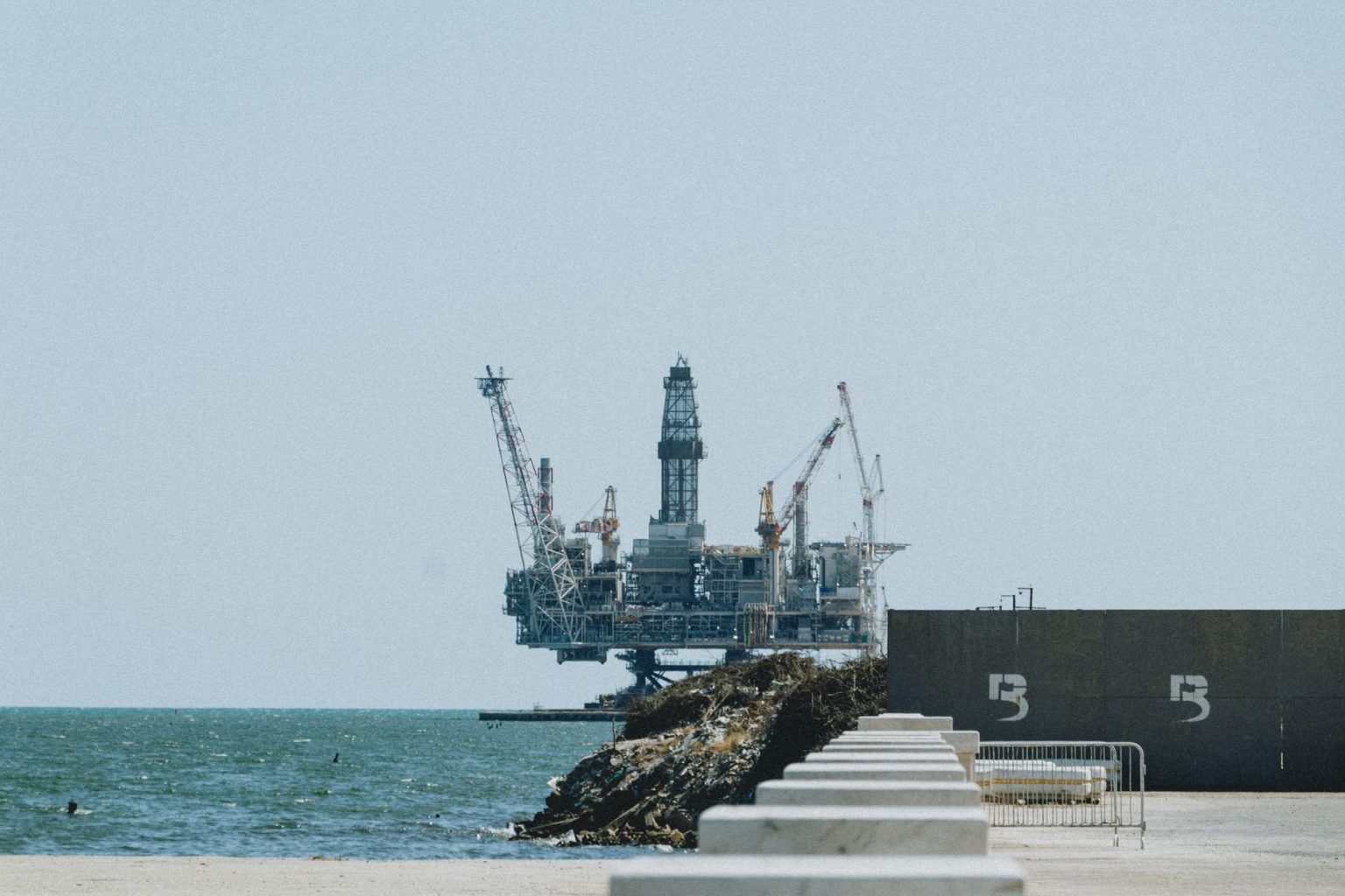 Plataforma de exploração de petróleo offshore com guindastes, vista ao longe em um dia ensolarado.